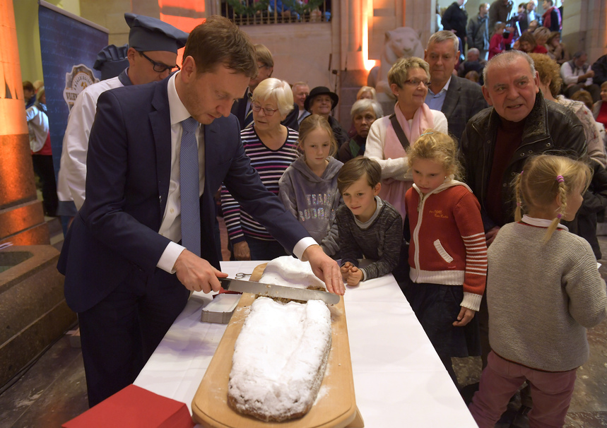 Ein Mann schneidet einen Stollen an. Kinder sehen ihm dabei zu.