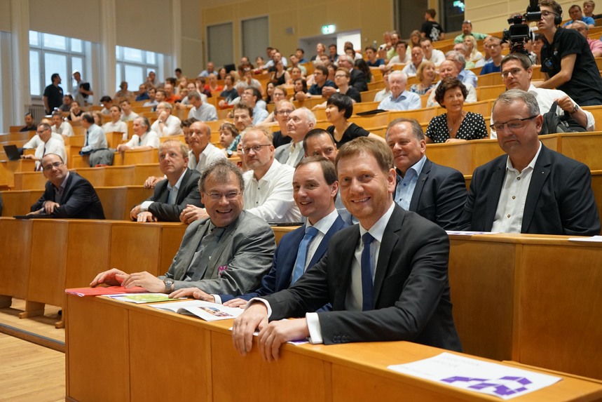 Männer und Frauen sitzen in einem Hörsaal auf den Sitzbänken.