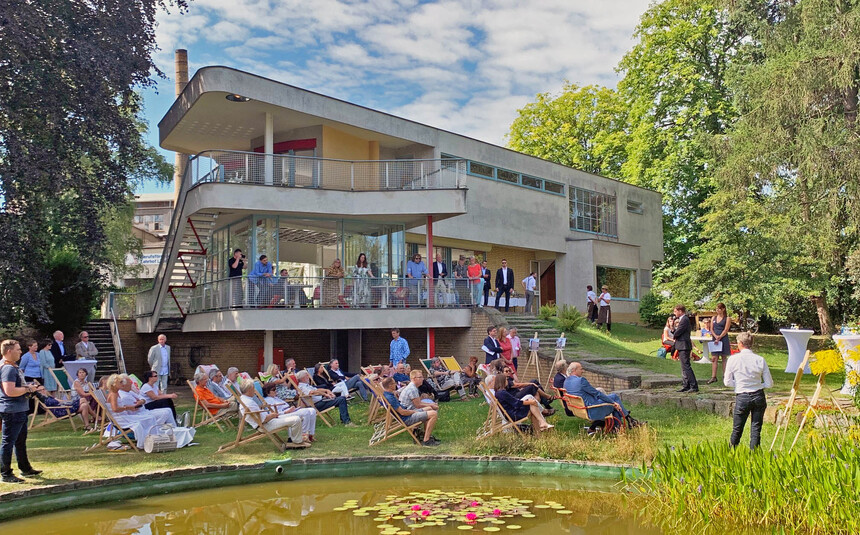 Männer und fRauen stehen im Garten vor einem Gebäude.