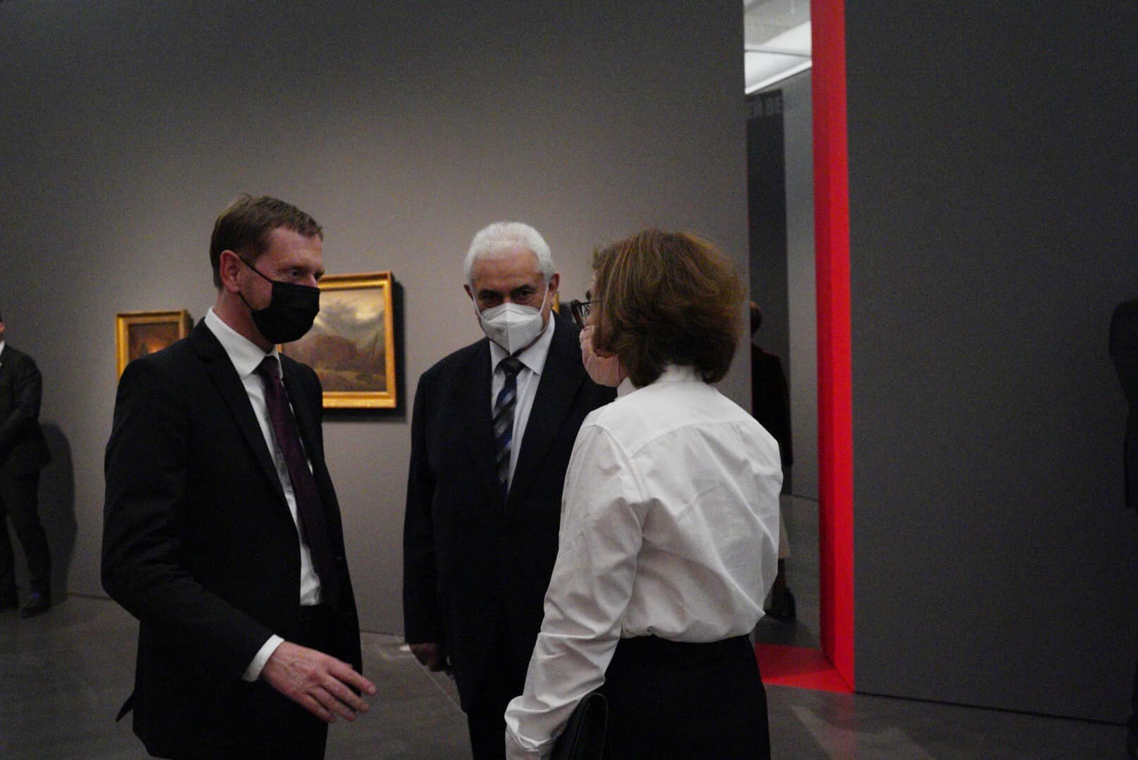 Zwei Männer und eine Frau unterhalten sich in einer Galerie.