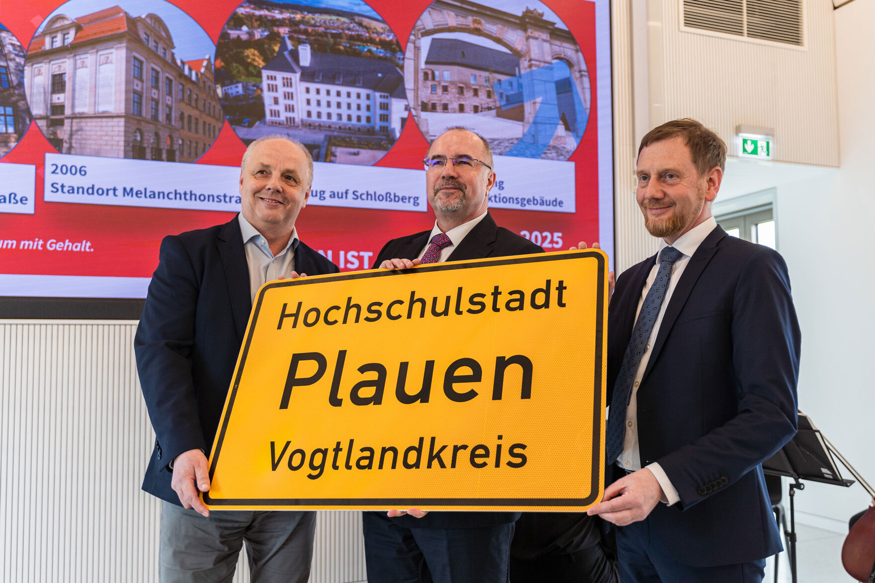 Drei Männer halten ein Ortseingangsschild mit der Aufschrift: »Hochschulstadt Plauen Vogtlandkreis« in Ihren Händen