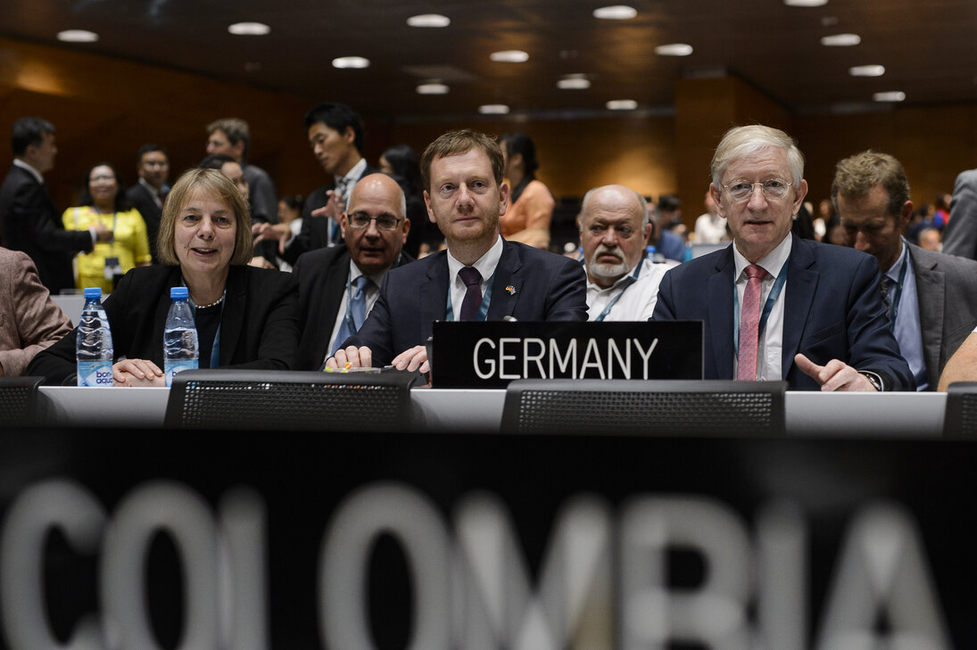 Mehrere Menschen sitzen hinter einem Tisch, auf dem »Germany« steht.