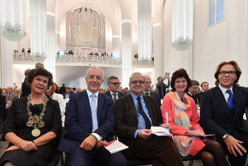 EIne Gruppe von Menschen sitzt nebeneinander in einer großen Aula.