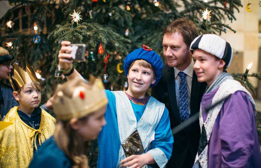 Ein Junge macht ein Selfie von sich und einem Mann im Anzug. Im Hintergrund steht ein Weihnachtsbaum.