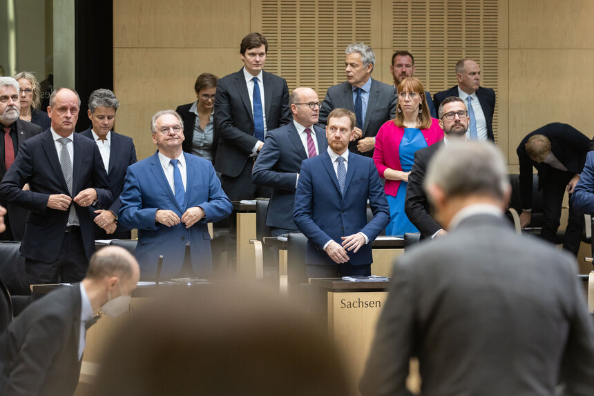 Mehrere Menschen stehen in einem Plenarsaal.