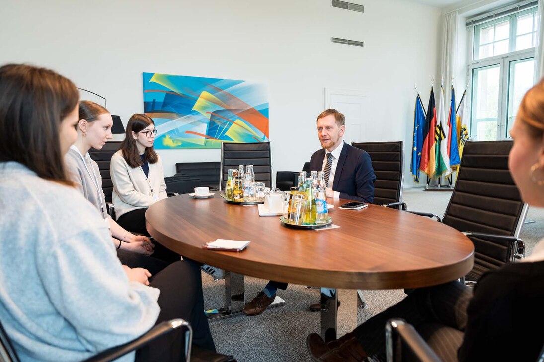 Vier Jugendliche und ein Mann sitzen an einem ovalen Tisch.