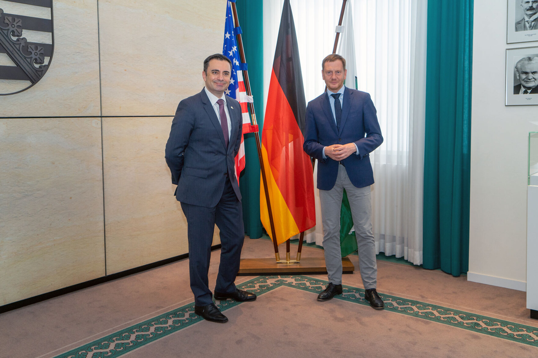 Zwei Männer stehen vor mehreren Flaggen.