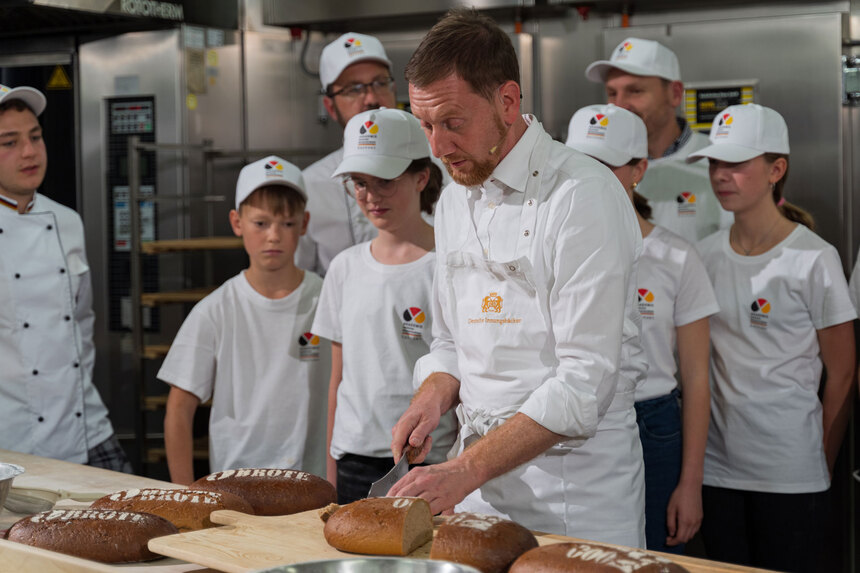 Ein Mann schneidet Brot und wird dabei von Kindern beobachtet.