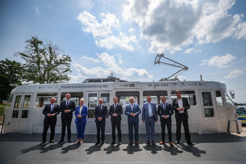 Männer und Frauen stehen in einer Reihe vor einer Straßenbahn.