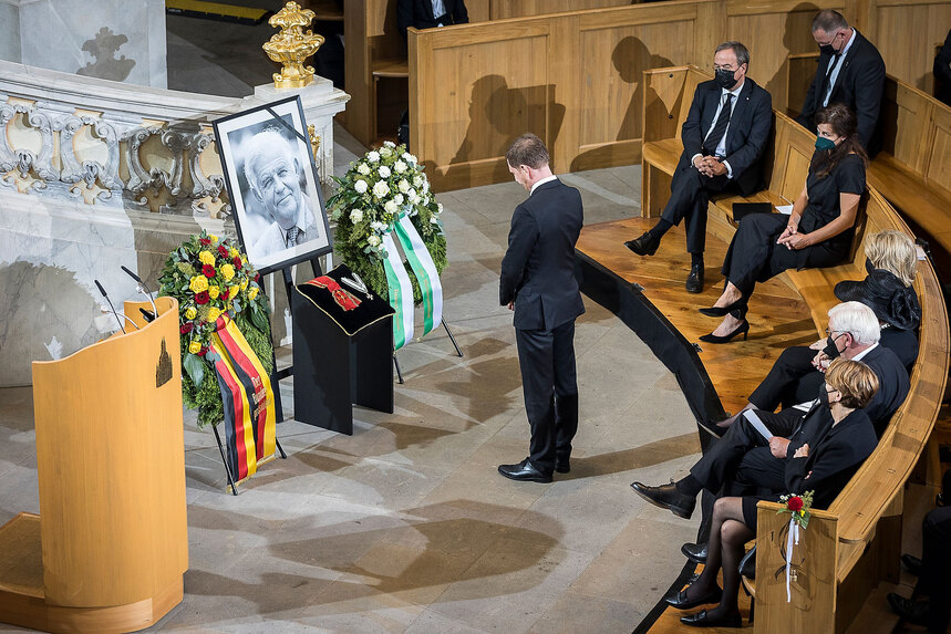 Ein Mann steht in einer Kirche vor einem Bild eines verstorbenen alten Menschen.