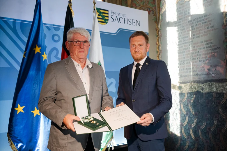 Ein Mann überreicht einem anderen Mann einen Orden.