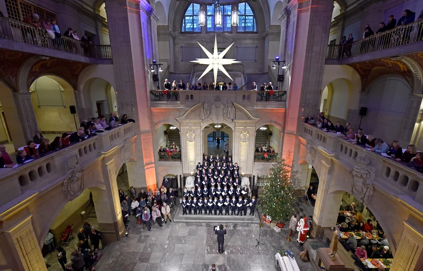 Viele Menschen stehen und sitzen versammelt in einer großen Halle vor einem Knabenchor.