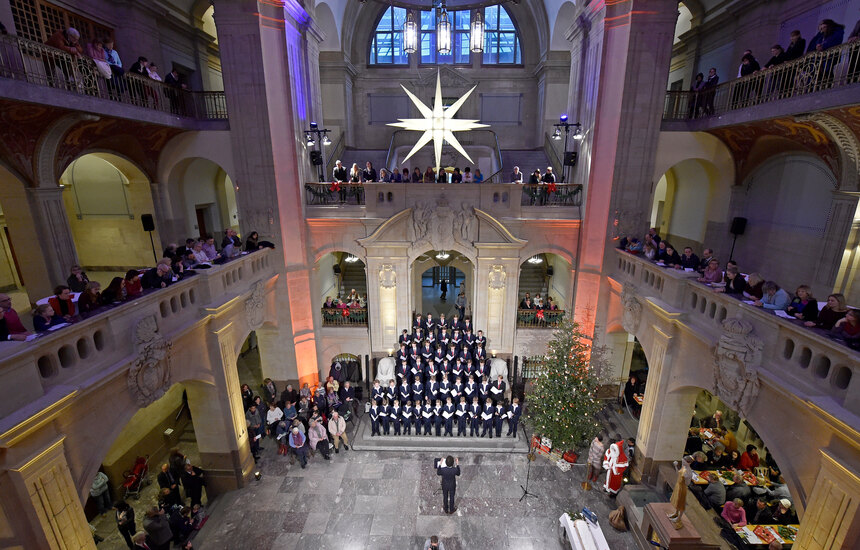 Viele Menschen stehen und sitzen versammelt in einer großen Halle vor einem Knabenchor.