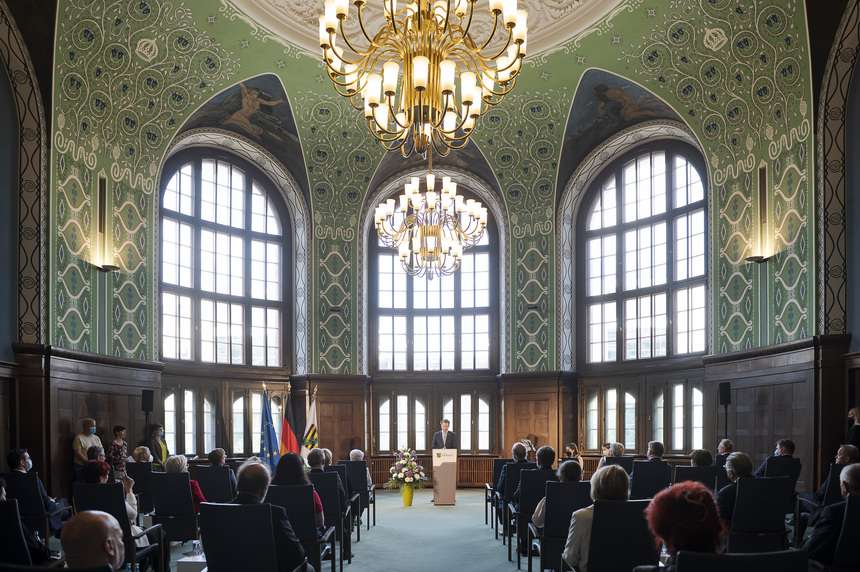 Menschen sitzen in einem großen Saal, in dem ein Kronleuchter an der Decke hängt.