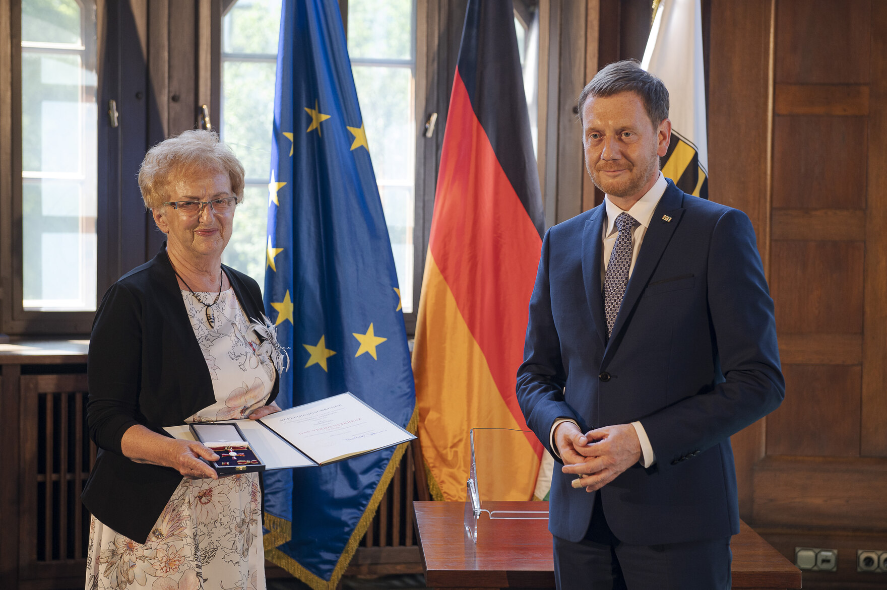 Eine Frau hält eine Urkunde in der Hand. Neben ihr steht ein Mann.