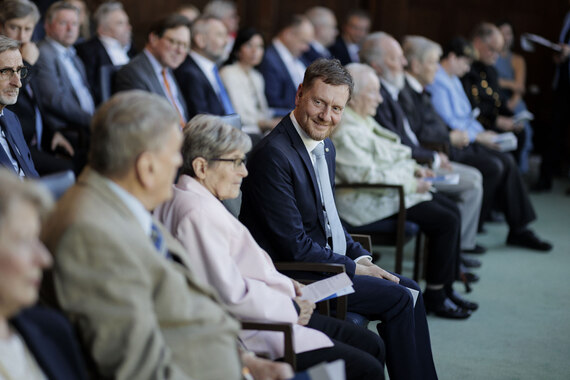 Männer und Frauen sitzen in einem großen Saal.