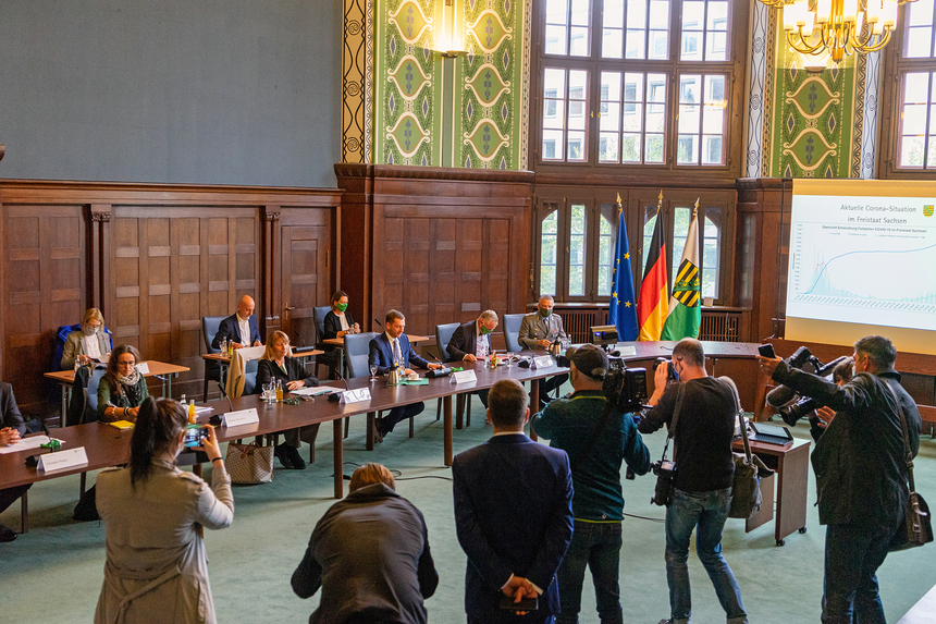 In einem Saal sitzen Männer und Frauen an einem Tisch. Vor Ihnen stehen Journalsiten, die sie fotografieren.