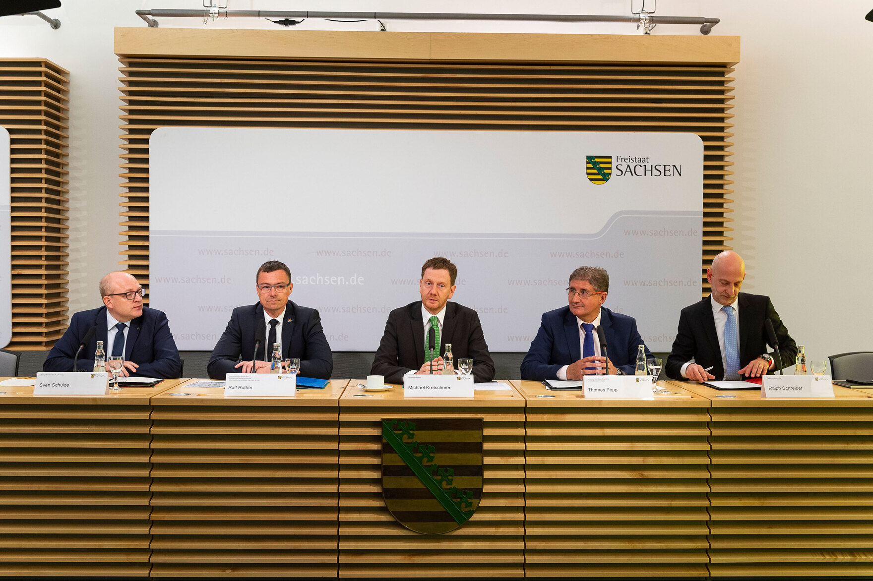 Männer siten auf einem Podium und halten eine Pressekonferenz.