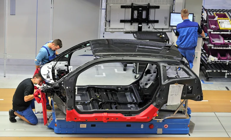 Drei Männer arbeiten an einer Fahrzeugkarosserie.