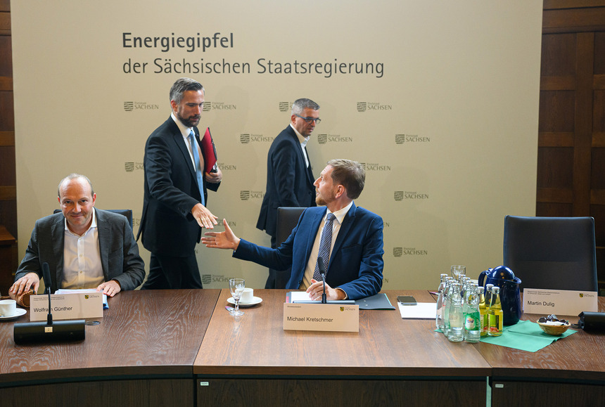 Männer sitzen an einem Tisch. Im Hintergrund steht eine Pressewand mit der Aufschrift Energiegipfel der Sächsischen Staatsregierung.