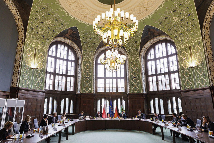 Männer und Frauen sitzen an einer Tafel in U-Form in einem großen Saal.