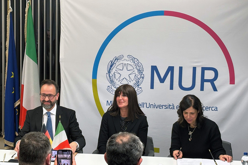 EIn Mann und zweii Frauen sitzen nebenainander an einem Konferenztisch.