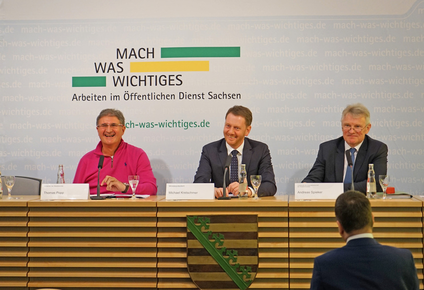 Männer sitzen auf einem Podium.