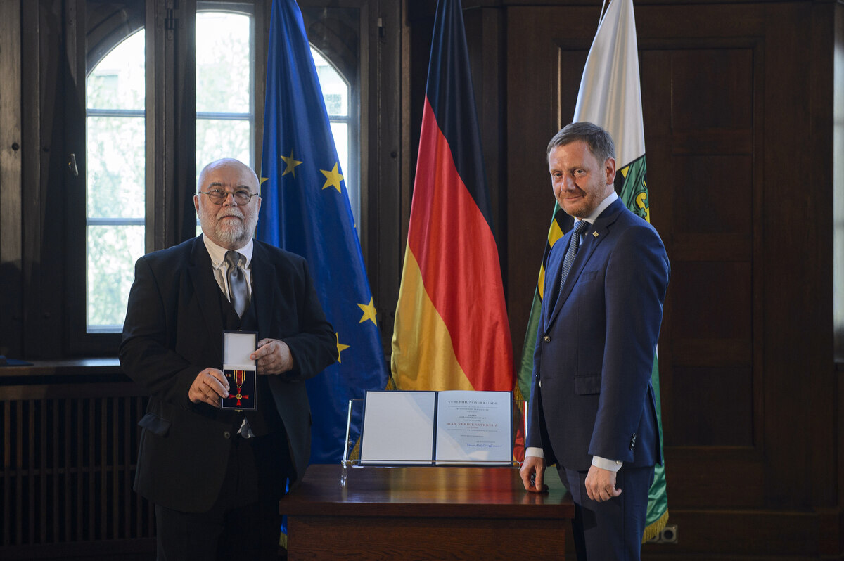 Zwei Männer stehen neben einem Pult. Einer hält einen Orden in der Hand.