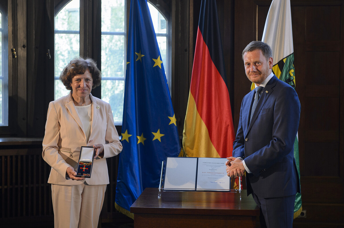 Ein Mann und eine Frau stehen neben einem Pult. Sie hält einen Orden in der Hand.