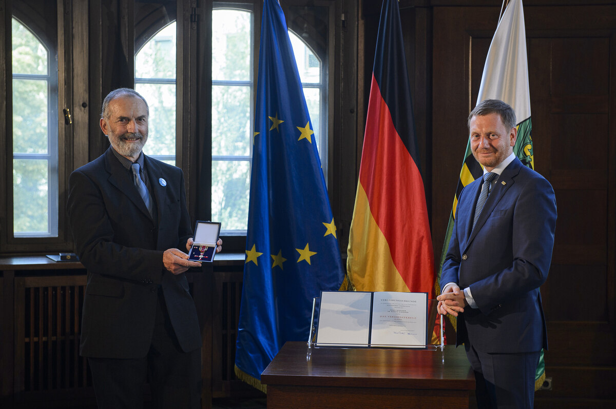 Zwei Männer stehen neben einem Pult. Einer hält einen Orden in beiden Händen.