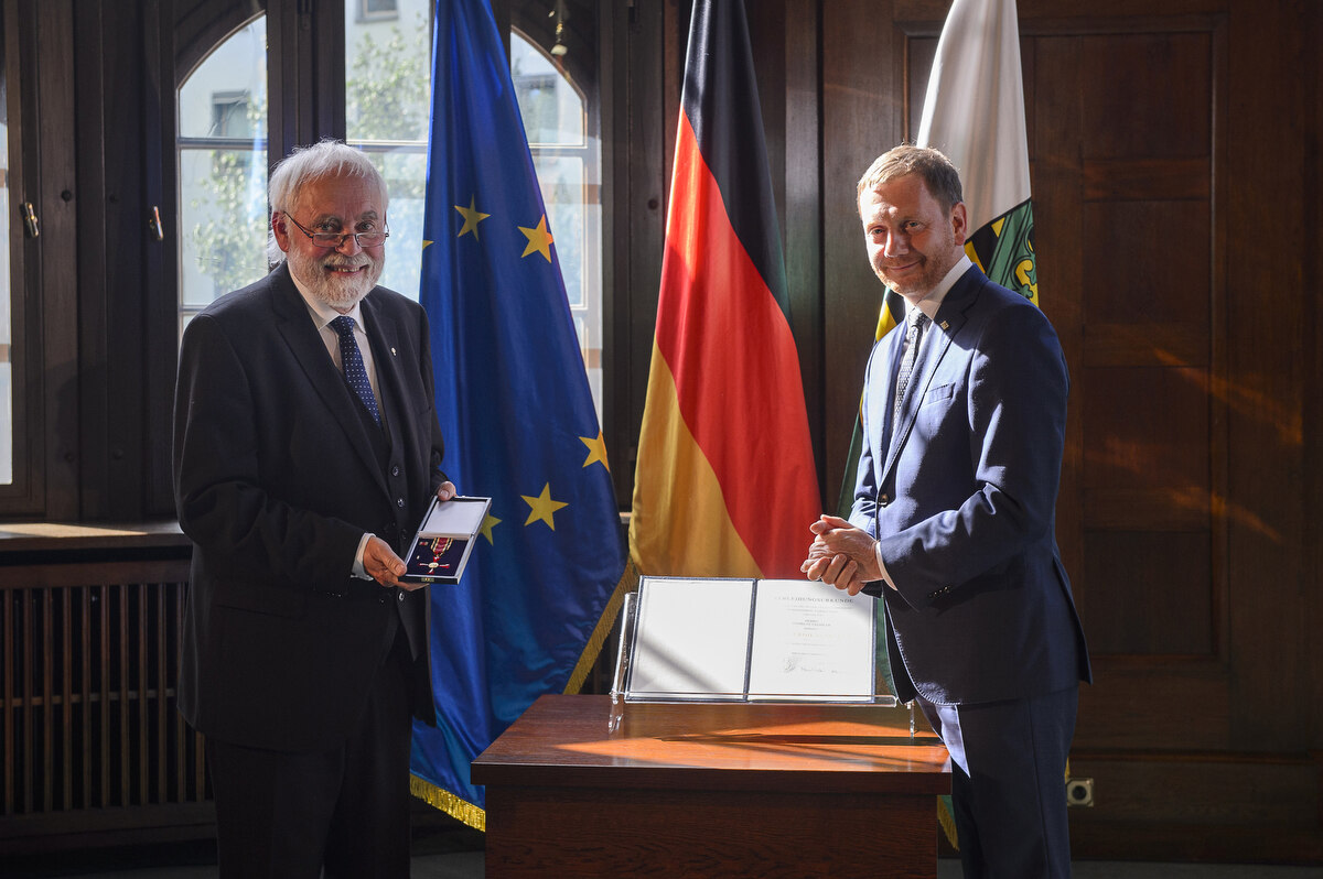 Zwei Männer stehen neben einem Pult. Ein Mann hält einen Orden in der Hand.