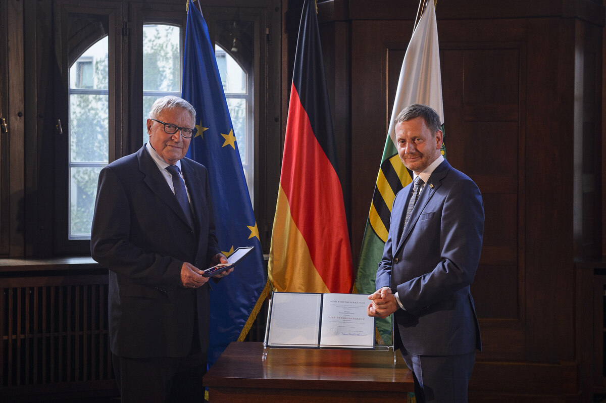 Zwei Männer stehen neben einem Pult. Einer von ihnen hält einen Orden in der Hand.