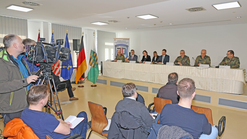 Männer sitzen an einem langen Tisch und halten ein Pressegespräch ab. Vor ihnen sitzen Journalisten.