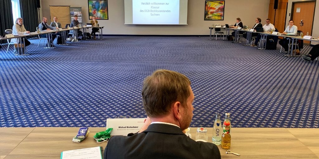In einem großen Konferenzraum sitzen Männer und Frauen an einem Tisch in U-Form.