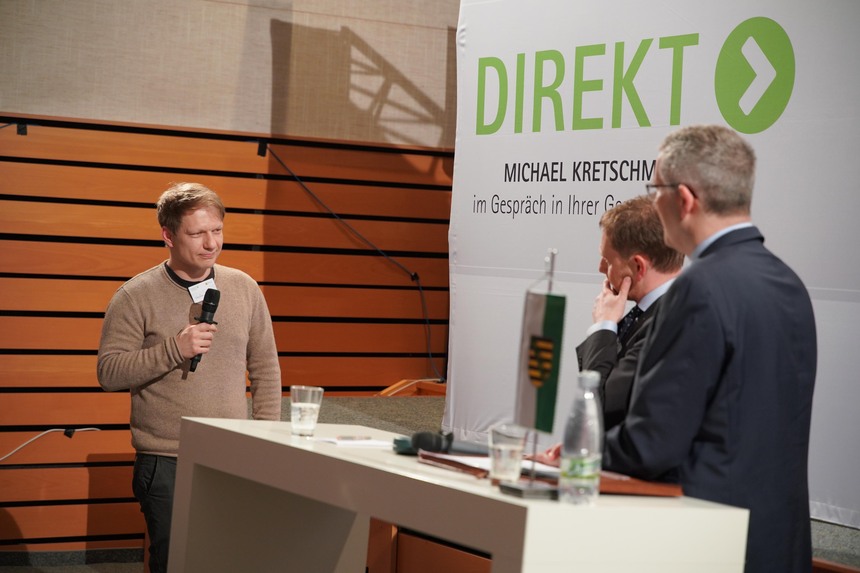 Zwei Männer hören einem Mann mit einem Mikrofon in der Hand zu.