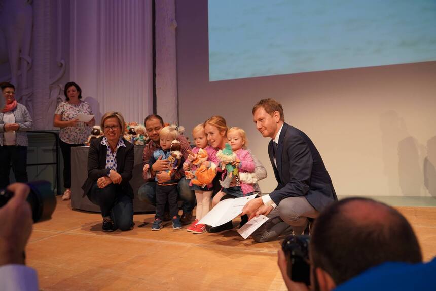 Ein Mann und eine Fraue sitzen mit Kindern auf einer Bühne.