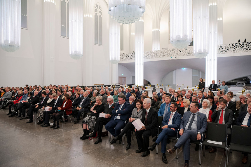 Männer und Frauen sitzen in einem Saal.