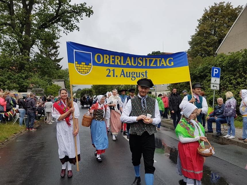 Männer und Frauen gehen in Trachten gekleidet eine Straße entlang.