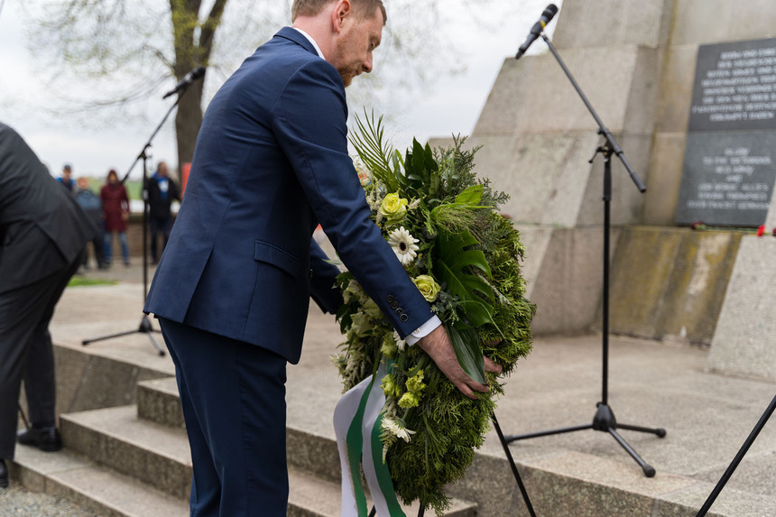 Ein Mann legt an einer Säule einen Kranz nieder.