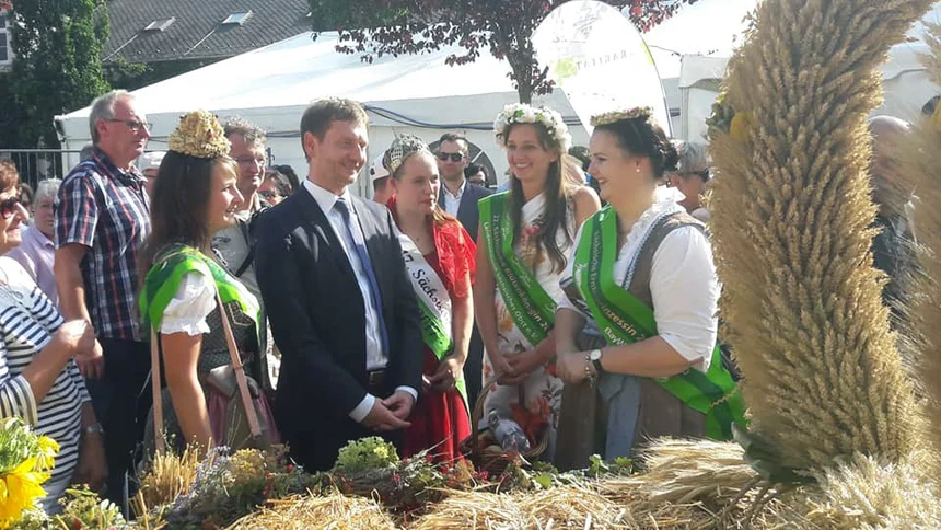 Männer und Frauen stehen vor einer Erntekrone.