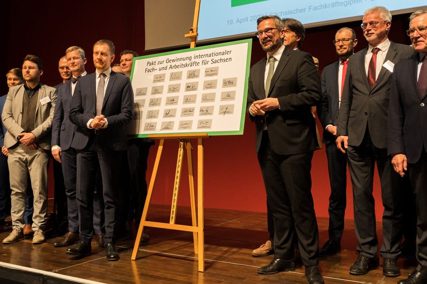 Männer stehen vor einer Pinnwand auf einer Bühne.