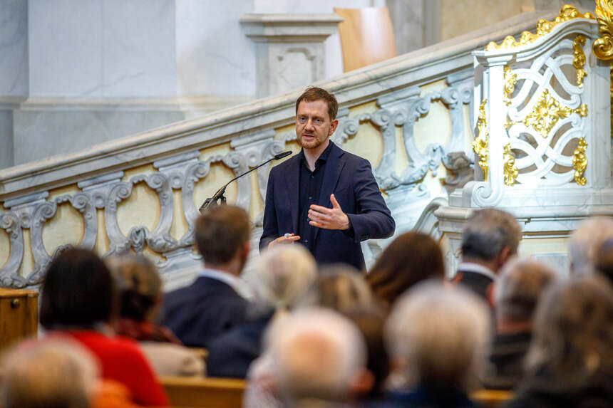 Ein Mann spricht an einem Pult vor einem Altar zu einem Publikum.