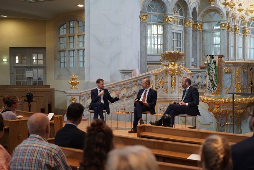 Männer sitzen vor einem Altar in einer Kirche und unterhalten sich.