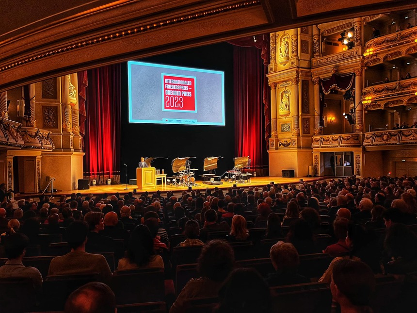 Ein Mann steht auf einer Bühne in einem großen Saal vor Publikum.