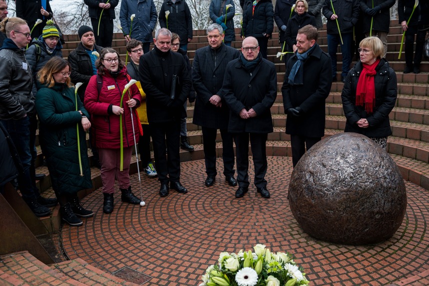 Männer und Frauen stehen vor einem Denkmal.