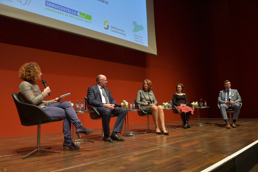 Männer und Frauen sitzen auf einem Podium.