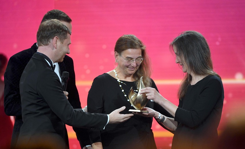 Ein Mann überreicht zwei Damen eine goldene Henne.