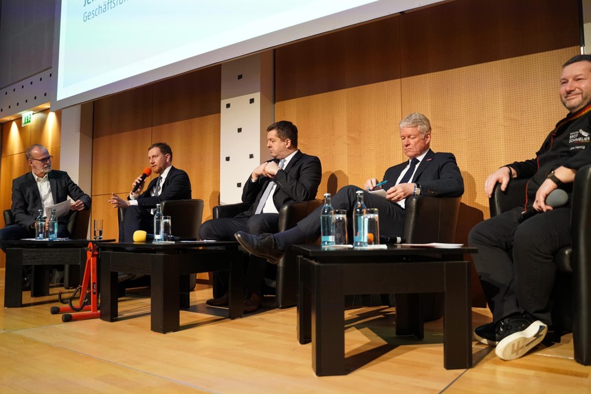 Männer sitzen auf einem Podium und sprechen in ein Mikrofon.
