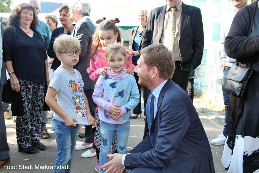 Ein Mann spricht kniend mit zwei Kindern.