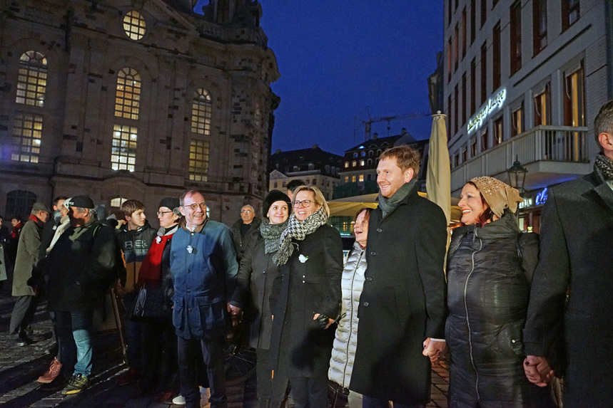 Männer und Frauen bilden vor einer Kirche eine Menschenkette.